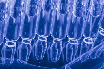 Glass medical ampoule vial for injection. Medicine is liquid sodium chloride with of aqueous solution in ampulla. Close up. Bottles ampule multicolor on background color and water. Human plasma.