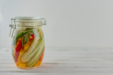 glass jar of fermented pumkin, cauliflower, cucumbers, onions, carrots, chili pepper. vegetables on a light background. fermentation is a source of probiotics