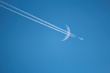 An Airplane is flying on the bright blue sky an crossing the waxing crescent moon
