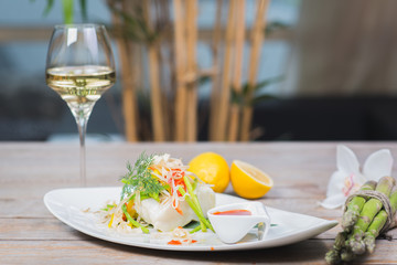 White fish seabass fillet with vegetables and white wine on a wooden table in a restaurant with decor. Tasty and healthy food. A cozy evening in a restaurant during a date. Beautiful table setting.
