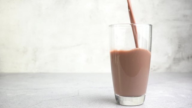 Close up pouring chocolate milk into a glass on the table.