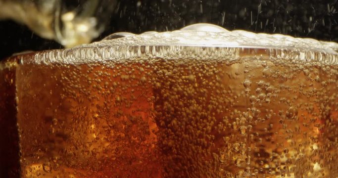 Refreshing Soda Drink Pouring with Bubbles Floating on Ice Cubes in a Glass a Macro Shot on Red with Black Background