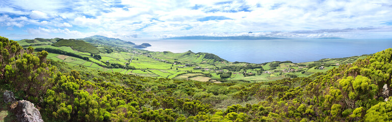 Large panorama from the Miradouro do Pico da Velha of the São Jorge countryside with the islands of Pico and Faial in the background. Pico summit is seen across the ocean under a dramatic cloudy sky. - obrazy, fototapety, plakaty