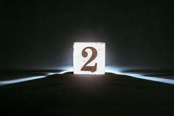 Number 2, two, on a wooden block - dark background