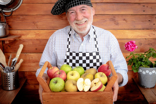 A smiling senior man holds a basket full of apples of various qualities and colors. Rustic background in recycled wood. One senior adult - Powered by Adobe