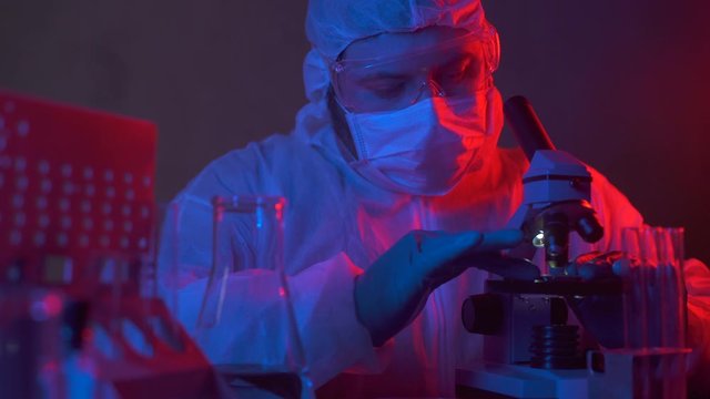 Scientist in hazard suit in electronic manufacturing factory research new device. New silicon electronic chip in the hands of a researcher in a dark lablaboratory. Cyber technology development.