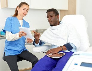 Cosmetician woman with papers talking to man before procedure in clinic