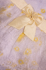 Beautiful yellow fabric bow on bright background with floral pattern. Closeup.