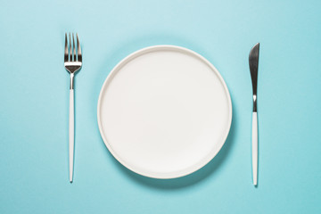 Table setting with white plate and cutlery on blue.