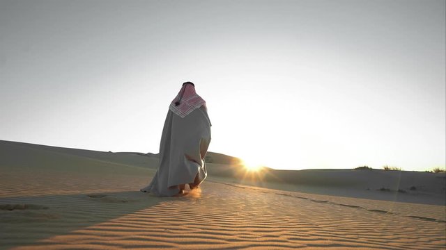 Arab walks through the desert at sunset alone Saudi Arabia IN NATIONAL CLOTHES the sun shines