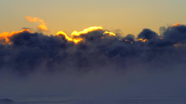 Massive clouds of Great Lakes fog backlit by the rising sun at twilight, seamless loop.