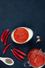 Hot chili pepper sauce paste harissa. Adjika on a blue background. Traditional Tunisia, Georgian and Arabic cuisine. Homemade rose harissa in a bowl.
