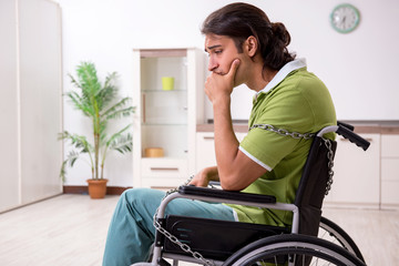 Young male invalid in wheel-chair suffering at home