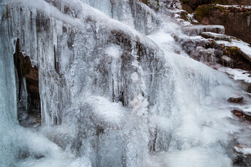 Amazing, close-up view of completely frozen waterfall, beautiful details of frozen water and icicles hanging from the cliff