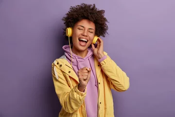 Poster Lets enjoy sound of music. Upbeat cheerful woman holds hand as microphone, sings song and heart out, listens uses modern headphones, has overjoyed expression, being real meloman, dressed casually © Wayhome Studio