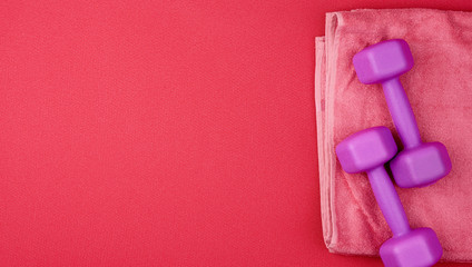 pair of purple plastic dumbbells and pink terry towel on a red neoprene mat
