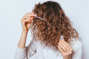 Young woman applying cosmetic oil to her beautiful curly hair
