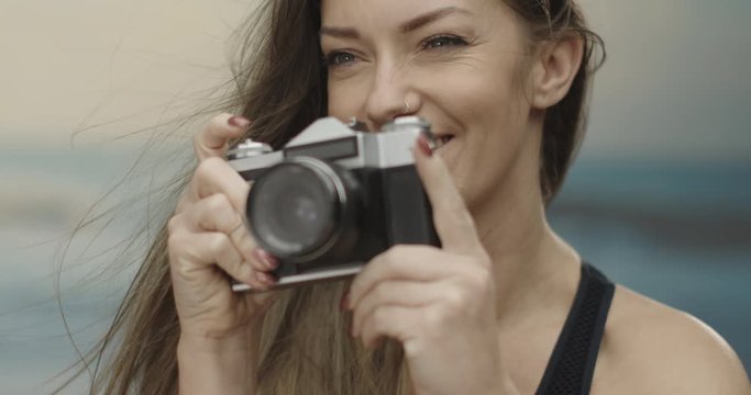 cute female photographer using her analogue camera at the beach. Sea in the background. Slow motion 4K