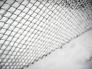 Beautiful winter scene, metal mesh covered with snow. The ground is also covered with snow.