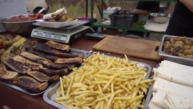 Showcase cafe at the fair with french fries and grilled vegetables: fried eggplant, bell pepper, zucchini. The customer picks up his finished order. Slow motion video