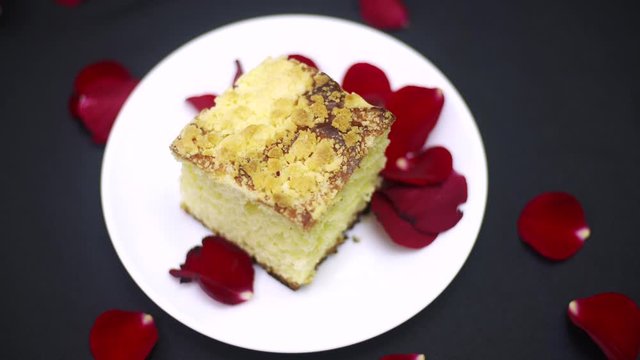 Ciasto drożdżowe na czarnym tle, posypany płatkami czerwonych r&oacute;ż