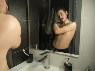 Portrait of handsome caucasian teenager reflection in from of the mirror, drying his hair with a black towel