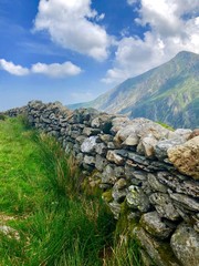 Fototapeta na wymiar Welsh landscape mountains, stone walls, gates, lake, blue skies and green grass in Wales