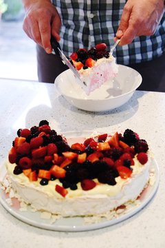 Midsection Of Man Holding Pavlova Cake Slice Over Bowl On Table