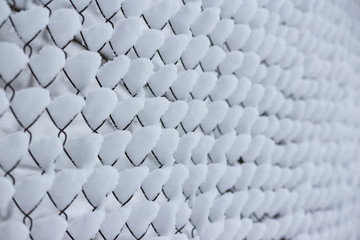 A piles of snow on the cells of the mesh fence. Snowfall in winter