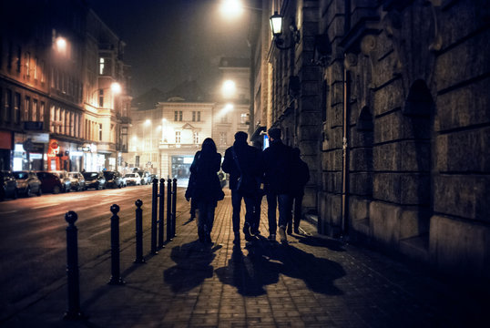 Rear View Of People Walking On Sidewalk At Night