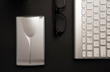 Conceptual table for informatic work, silver-colored desktop hard drive with lenses, partial view of computer keyboard, black background