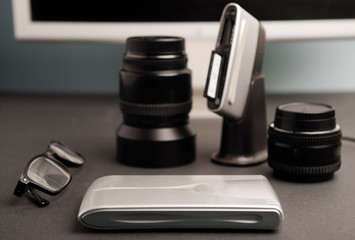 concept work table photographer, composition, silver-colored desktop hard drive with spectacles, 80mm photographic lens, compacflash cards downloader, 50mm photographic lens, partial computer view