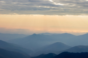 Fototapeta na wymiar Soft, colorful view of distant mountain layers in Bulgaria from Old mountain in Serbia, lighten by morning sun rays under dramatic, vibrant sunrise sky