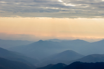 Fototapeta premium Soft, colorful view of distant mountain layers in Bulgaria from Old mountain in Serbia, lighten by morning sun rays under dramatic, vibrant sunrise sky