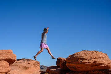 Naklejka premium Woman Jumps Over Sandstone Boulders