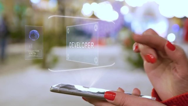 Female hands interact with HUD hologram text Developer. Woman with red nails and sweater uses the holographic technology of the future in the smartphone screen on the background of street
