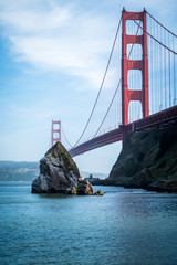 The iconic Golden Gate Bridge from a unique angle with a rock standing jutting out of the Bay water on a summer day. Taken from Sausalito, California in Marin County across the Golden Gate Strait 