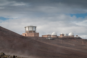 Obraz premium Haleakala Volcano, Maui, Hawaii, USA. - January 13, 2020: Observatory buildings and University of Hawaii facilities on top near the crater under cloudscape with blue patches.