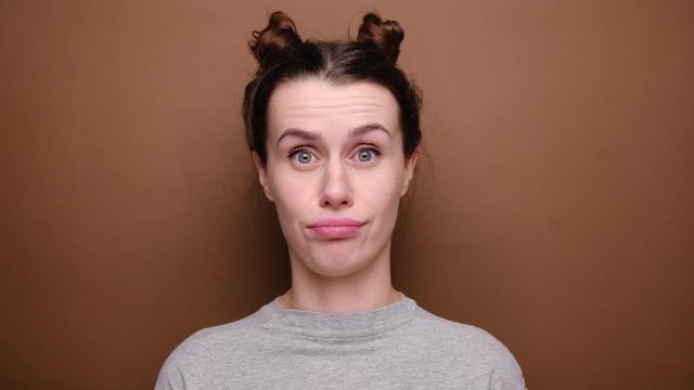 Cute young woman makes funny face, crosses eyes and sticks out tongue, plays fool, doesnt want to be responsible and looking at camera, stands over brown background. Positive emotions