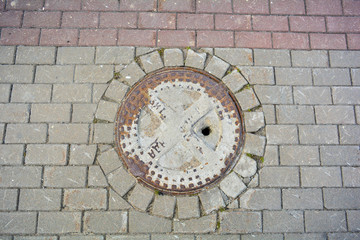 Ancient cast iron rusty manhole on pavement sidewalk of city street