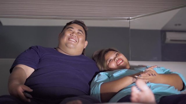 Happy obese couple watching TV together at night in the bedroom. Shot in 4k resolution