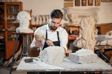 Stone carver works with wooden hammer and chisel at limestone.