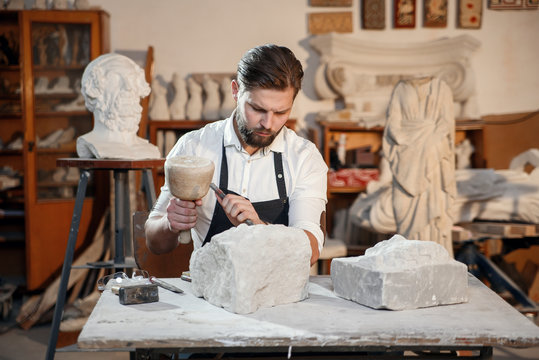 Stone carver works with wooden hammer and chisel at limestone.