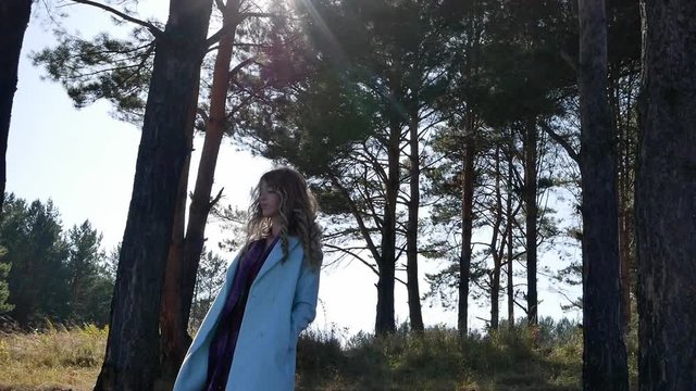 Beautiful young woman in blue coat standing in forest in windy weather autumn Sunny day