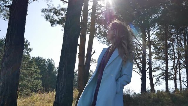 Beautiful young woman in blue coat standing in forest in windy weather autumn Sunny day