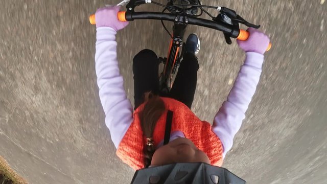 Pov view. One caucasian children rides bike road in autumn park. Little girl riding black orange mtb cycle in forest. Kid goes do bicycle sports. Biker motion ride with backpack and helmet.