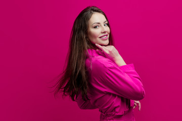 Obraz premium Cute and cheerful young brunette in a pink suit on a pink background