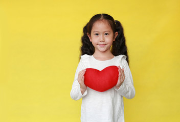 Portrait of smiling asian kid girl holding a red heart for you isolated on yellow background with copy space.