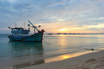 Fototapeta na wymiar Fishing boat on a deserted beach on sunset background