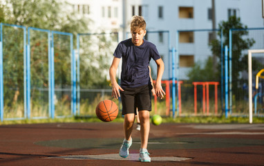 Cute smiling boy in blue t shirt plays basketball on city playground. Active teen enjoying outdoor game with orange ball. Hobby, active lifestyle, sport for kids.	